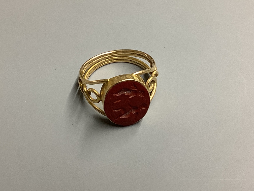 A yellow metal and carved oval Jasper set signet ring, with pierced shank, the matrix carved with two cherubs, size O gross 3.7 g.